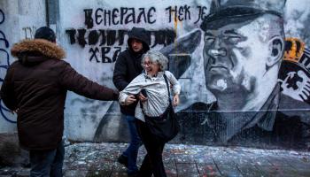 رجُلا أمن بملابس مدنية يعتقلون ناشطةً قذفت جدارية مُجرم الحرب ملاديتش في بلغراد بالبيض، 9 تشرين الثاني/ نوفمبر 2021 (Getty)