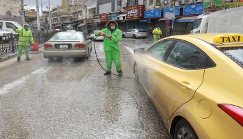 عمال البلدية يرشون السيارات بالمطهرات في عمان ( Getty)